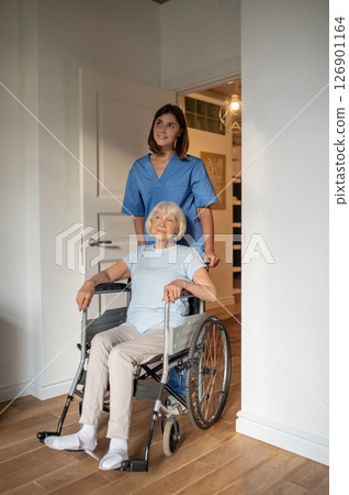 Young female nurse carrying a wheelchair with an elderly woman 126901164