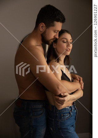 Shirtless man in jeans embracing woman in black top and jeans standing closely in intimate moment Shirtless man in jeans embracing woman in black top and jeans standing closely in intimate moment 126901227