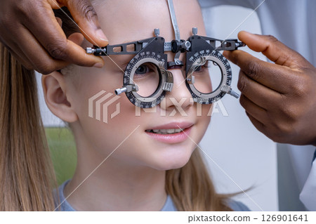 Doctor adjusting optometric tool while testing vision of a girl Doctor adjusting optometric tool while testing vision of a girl 126901641