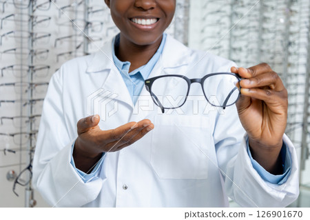 Smiling dark-skinned optician presenting new model of eyeglasses 126901670