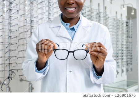 African american optometrist in a lab coat holding new eyeglasses in hands African american optometrist in a lab coat holding new eyeglasses in hands 126901676
