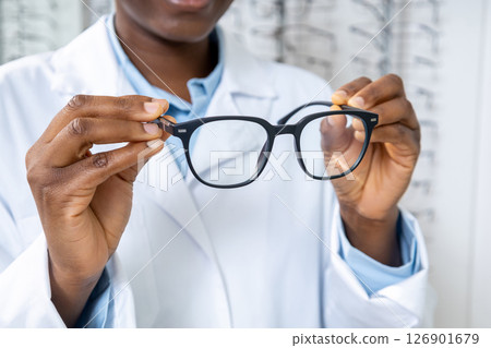 African american optometrist in a lab coat holding new eyeglasses in hands African american optometrist in a lab coat holding new eyeglasses in hands 126901679
