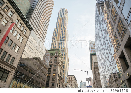 A modern glass skyscraper rises above historic and contemporary buildings in Midtown Manhattan. Reflections, vertical lines, and soft morning light highlight the architectural contrast. A modern glass skyscraper rises above historic and contemporary buildings in Midtown Manhattan. Reflections, vertical lines, and soft morning light highlight the architectural contrast. 126901728
