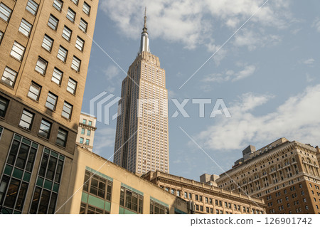 The iconic Empire State Building towers above surrounding structures. The photo captures its pointed spire and detailed windows on a clear day. The iconic Empire State Building towers above surrounding structures. The photo captures its pointed spire and detailed windows on a clear day. 126901742