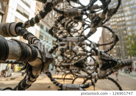 A close-up of an intricate metal sculpture in an urban setting. The background reveals modern buildings and city life. A close-up of an intricate metal sculpture in an urban setting. The background reveals modern buildings and city life. 126901747