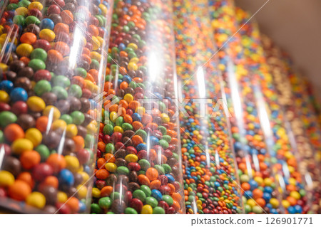 Rows of transparent tubes filled with candies in multiple colors. A bright and playful candy wall inside the store. Rows of transparent tubes filled with candies in multiple colors. A bright and playful candy wall inside the store. 126901771