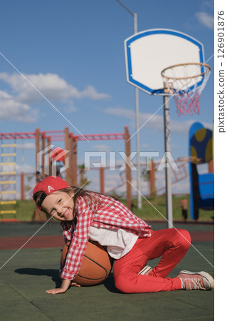 Funny funky girl in a baseball cap playing with a basketball on the playground 126901876