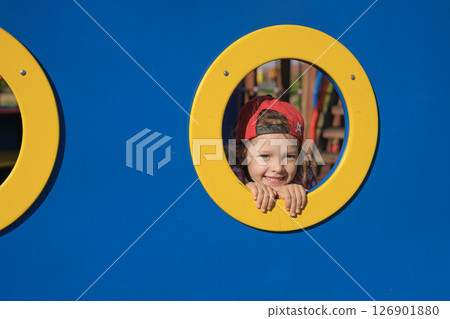 Funny girl peeks through a hole in the playground 126901880