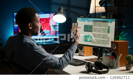 Black economist on video conference chat with consultants analyze earnings balance and tracking financial fluctuation for a potential growth. Specialist debating with his associates. Camera B. Black economist on video conference chat with consultants analyze earnings balance and tracking financial fluctuation for a potential growth. Specialist debating with his associates. Camera B. 126902711