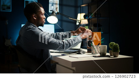 Independent freelancer creates a post it reminder and reviews project data, doing handwritten notes and placing sticky notes to remember his remote tasks. Researching articles. Camera A. 126902723