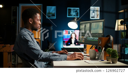 Young man video editor works on editing film footage at home setup, doing freelance contract for post production scenes. Editor correcting white balance and color grading, pc software. Camera A. 126902727