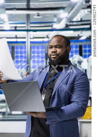 Factory employee checking solar panel machinery and reviewing a checklist, playing a vital role in renewable energy production and assembly line. Efficient solar tech infrastructure. 126902745