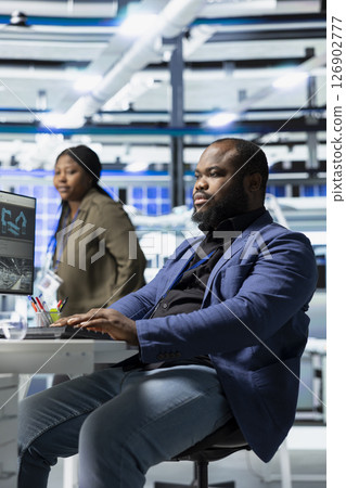 Black clean energy technician in suit checks solar panel alignment, representing the skilled workforce behind industrial operations for renewable energy development and production. 126902777