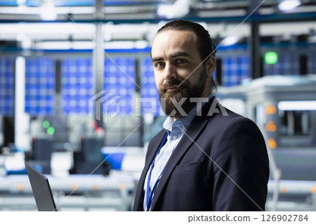 Factory inspector in a suit monitoring solar panel production output, reflecting professional occupation and executive level involvement in renewable energy development. Solar power. Factory inspector in a suit monitoring solar panel production output, reflecting professional occupation and executive level involvement in renewable energy development. Solar power. 126902784