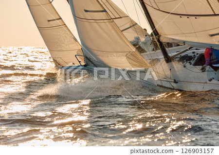 Sailing regatta in the Gulf of Finland at sunset, the bows of two sailing yachts competing in a race, splashing water from under the boats, teamwork, board the boat 126903157