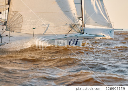 Sailing regatta in the Gulf of Finland at sunset, the bows of two sailing yachts competing in a race, splashing water from under the boats, teamwork, board the boat 126903159