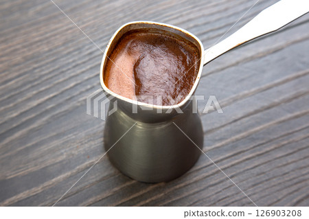 Close-up of a traditional metal cezve with rich Turkish coffee on a wooden table 126903208