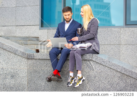 businessmen man and woman sitting on the stairs of a business building with documents and a laptop  126903228