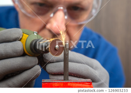 Male locksmith worker processes metal with engraving drill cutting.  126903233