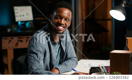 African American freelancer working from home writing notes and researching data driven topics. Focused on productivity and planning tasks in a modern apartment for remote work success. Camera B. 126903362