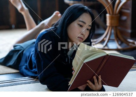 A high school girl lying down and reading a book 126904537