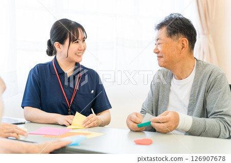 一位老人與一位在養老院或護理機構工作的女性護理人員一起摺紙 126907678