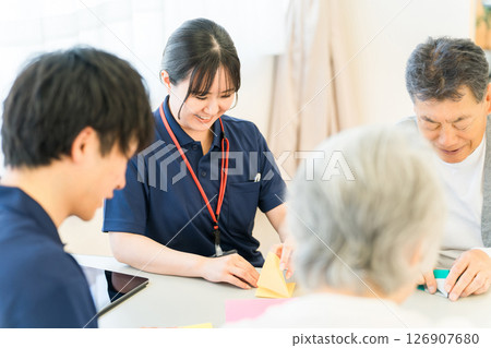養老院或護理機構的老年男女與男性和女性護理人員一起摺紙 126907680