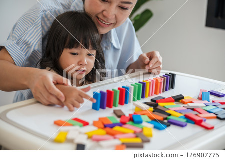 toddler girl and mother playing colorful wooden block toy or domino game together toddler girl and mother playing colorful wooden block toy or domino game together 126907775