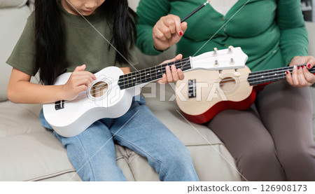 Music Education at Home. A young girl learns to play the ukulele with her mother's guidance. 126908173