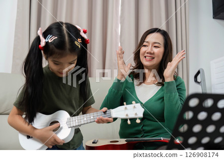Joyful Music Lesson. Young girl learning ukulele with supportive mother at home. 126908174
