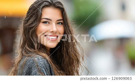 Cheerful young woman with wet hair smiling in the rain on a city street. Natural look, soft daylight, outdoor urban background. Cheerful young woman with wet hair smiling in the rain on a city street. Natural look, soft daylight, outdoor urban background. 126909063
