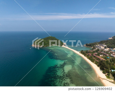 A lush green island surrounded by turquoise waters and a sandbar under a sunny sky, with visible coral reefs. Ko Pha Ngan, Thailand. 126909402