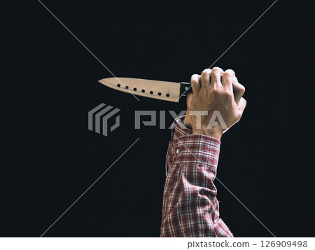 Close-up of male hand in red plaid shirt gripping large kitchen knife raised in threatening position against dark background Close-up of male hand in red plaid shirt gripping large kitchen knife raised in threatening position against dark background 126909498