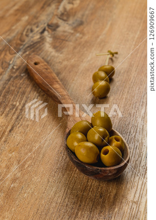 Wooden spoon filled with green olives on a rustic wooden table Wooden spoon filled with green olives on a rustic wooden table 126909667