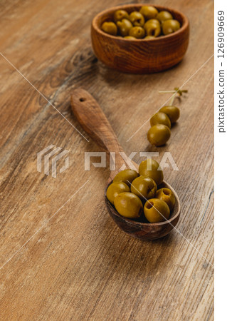Olives arranged in a wooden spoon on a rustic wooden table 126909669