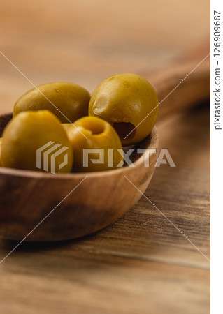 Green olives placed on a wooden spoon with warm background texture 126909687