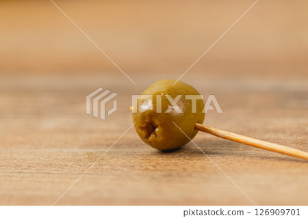Olive on a toothpick resting on wooden surface in natural light 126909701