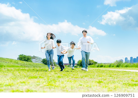 Family running through a grassland with blue sky 126909751