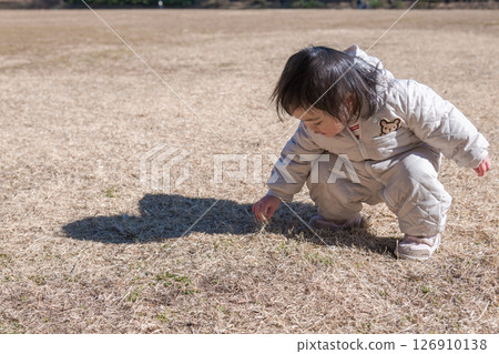 [One-year-old child crouching down while playing on the grass at Sagamihara Municipal Asamizo Park] 126910138