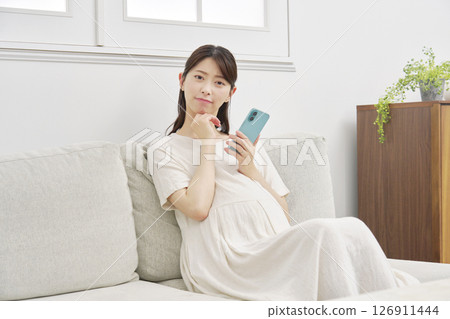 Pregnant woman thinking with smartphone in living room 126911444
