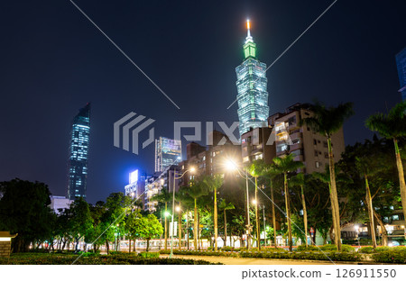 In Taipei, Taiwan, a glowing bamboo inspired tower rises with nearby high rises above a palm lined park and boulevard on a clear night. 126911550