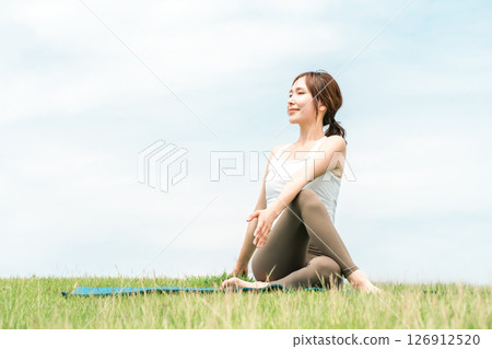 A woman meditating, doing yoga, stretching and pilates in the grassland (healthcare and diet) 126912520