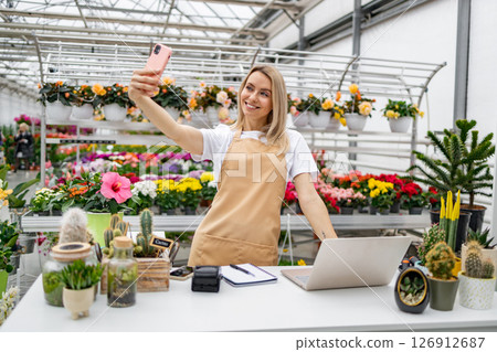 A Caucasian woman takes a selfie in her florist shop, surrounded by vibrant flowers and plants. 126912687