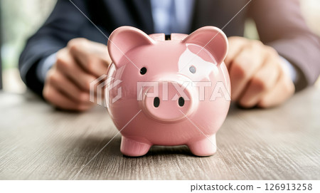 businessman is focused on saving money with pink piggy bank on wooden table, symbolizing financial planning and security businessman is focused on saving money with pink piggy bank on wooden table, symbolizing financial planning and security 126913258