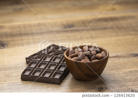 Cocoa beans and chocolate bar in wooden bowl on wooden table with copy space 126913620