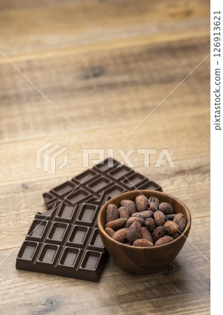 Cocoa beans and chocolate bar in wooden bowl on wooden table with copy space 126913621