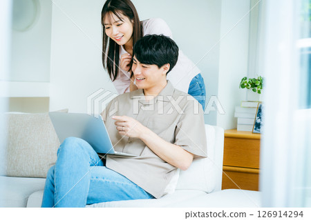 A couple looking at a computer in the living room 126914294