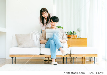 A couple looking at a computer in the living room A couple looking at a computer in the living room 126914296