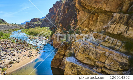 Aerial Fly Through Rugged Desert Canyon with Sunlit Rock Face and Winding River 126914892