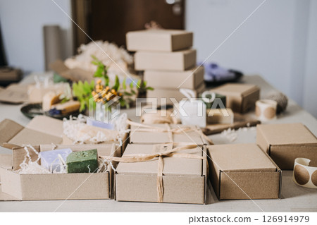 Table filled with kraft spa gift boxes containing handmade soaps and natural fillers. Spa gift box, handmade wellness products, calming rituals, stress relief gifts 126914979